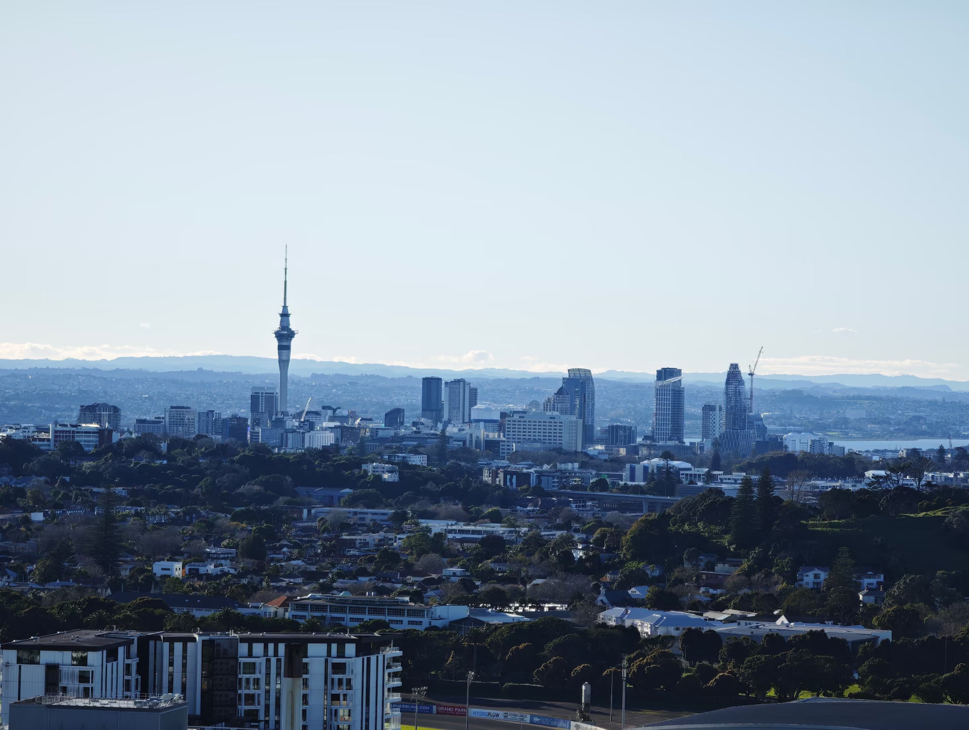 Panoramic view of the Auckland skyline at dawn, featuring the Sky Tower rising above office buildings and distant hills.